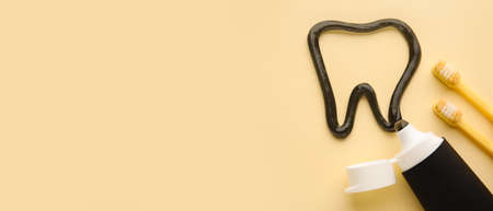 Tooth made of activated charcoal tooth paste and brushes on yellow background with space for textの写真素材
