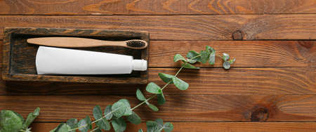Tube with toothpaste, brush and eucalyptus branch on wooden background