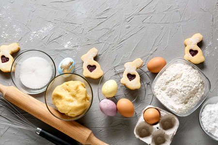 Bowl with fresh dough, painted eggs and ingredients for preparing Easter cookies on gray backgroundの写真素材