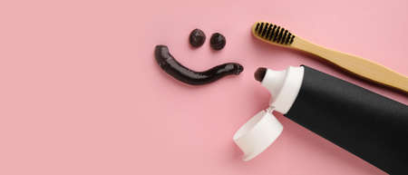 Smile made of activated charcoal tooth paste and brush on pink background with space for text