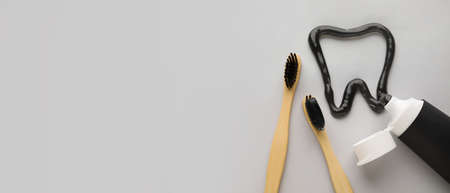 Tooth made of activated charcoal tooth paste and bamboo brushes on light background with space for textの写真素材