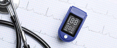 Pulse oximeter and stethoscope on cardiogram, top view
