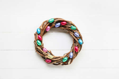 Easter wreath decorated with chocolate eggs on light wooden background