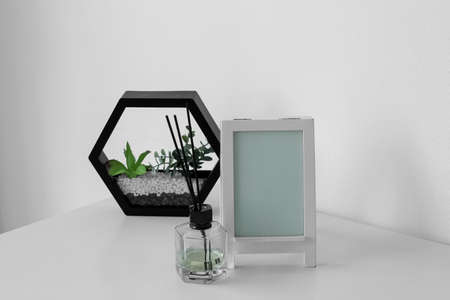 Blank frame, reed diffuser and planter on table near light wall
