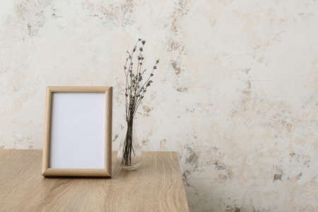 Blank frame and vase with flowers on table near light wallの写真素材