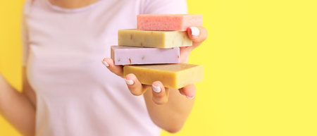 Young woman holding soap bars on yellow background with space for text, closeup