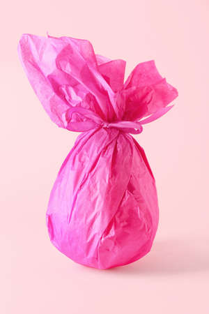 Chocolate Easter egg wrapped in paper on pink background