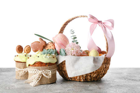 Gift basket with painted Easter eggs, flowers and cakes on table against white backgroundの写真素材