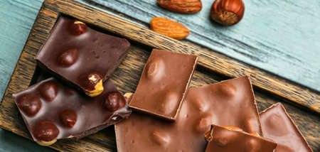 Pieces of tasty chocolate with hazelnuts and almonds on wooden table, closeup