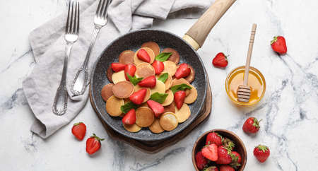 Composition with frying pan of tasty mini pancakes, strawberry and honey on light backgroundの写真素材