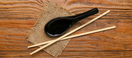 Spoon of soy sauce and chopsticks on wooden background, top viewの写真素材
