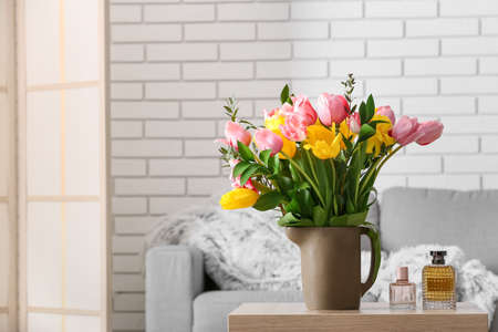 Vase with spring flowers and bottles of perfume on table in living roomの写真素材