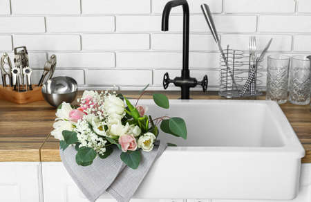 Sink with beautiful flowers and kitchenware on counters near white brick wall, closeupの写真素材