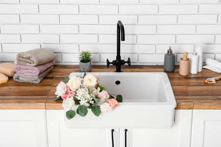 Sink with beautiful flowers and bath supplies on counters near white brick wallの写真素材