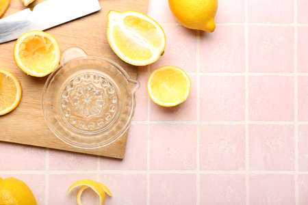 Wooden board with juicer and ripe lemons on color tile