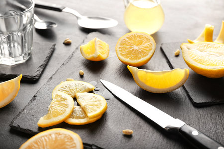 Board with pieces of juicy lemons and knife on dark background, closeupの写真素材