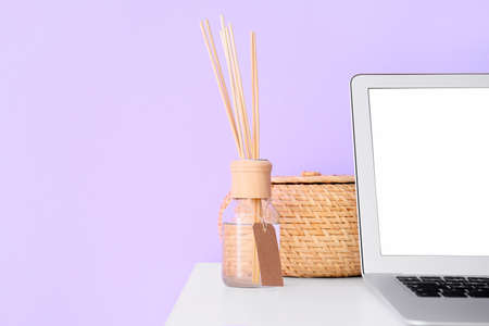 Reed diffuser, basket and laptop on table near lilac wall, closeupの写真素材