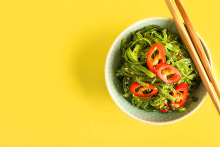 Bowl with healthy seaweed salad and chili pepper on yellow backgroundの写真素材
