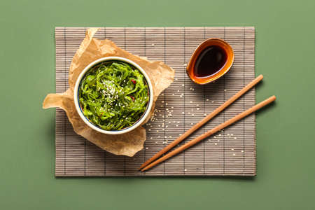 Bowl with healthy seaweed salad and sauce on green background