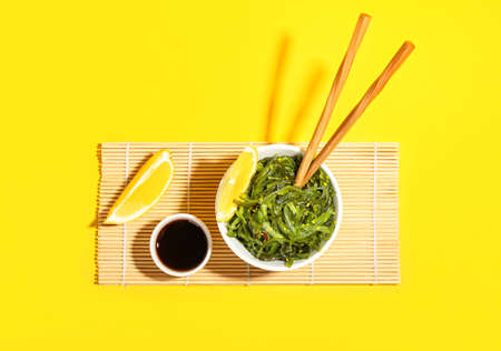 Bowl with healthy seaweed salad on yellow background