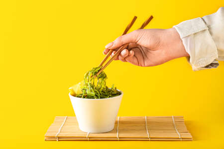 Woman eating healthy seaweed salad with chopsticks on yellow backgroundの写真素材