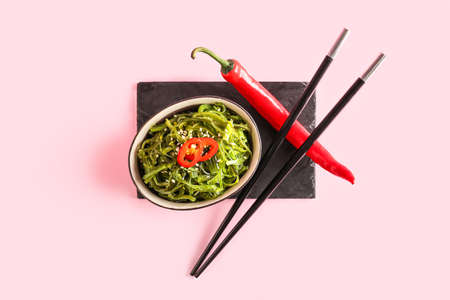 Bowl with healthy seaweed salad and chili pepper on pink backgroundの写真素材