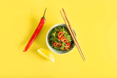 Bowl with healthy seaweed salad and chili pepper on yellow backgroundの写真素材