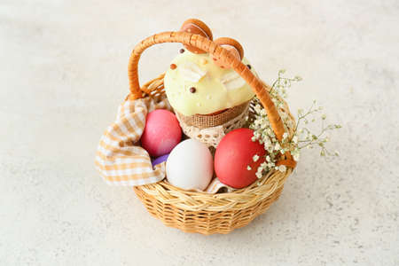 Gift basket with painted Easter eggs, flowers and cake on light background