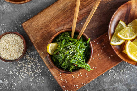 Bowl with healthy seaweed salad, lemon and sesame on gray grunge background