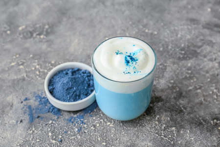 Glass of blue matcha tea and bowl with powder on gray grunge background