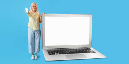 Mature woman with smartphone and big laptop on blue backgroundの写真素材