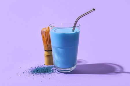 Glass of blue matcha tea, chasen and powder on purple backgroundの写真素材