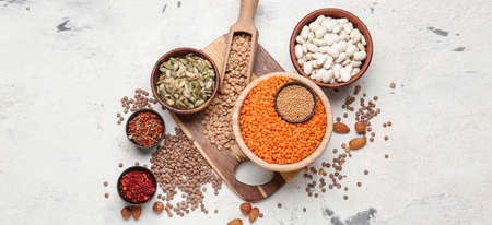 Bowls with raw legumes and spices on light background