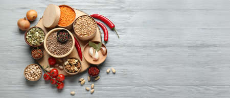 Different raw legumes with spices and nuts on gray wooden background with space for text
