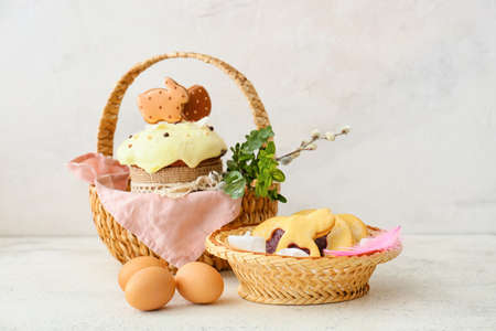 Gift baskets with Easter eggs, cake and cookies on light background