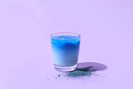 Glass of blue matcha tea and powder on purple backgroundの写真素材