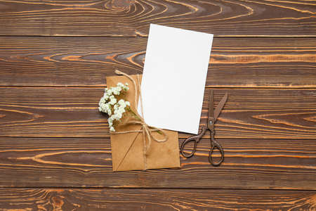 Envelope with card, scissors and flowers on wooden background