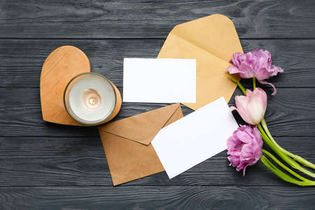 Envelope with blank cards, candle and flowers on dark wooden background