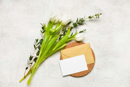 Envelope with blank card, eucalyptus branches and flowers on light background
