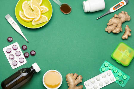 Frame made of medications for sore throat, lemon slices, ginger and thermometers on green backgroundの写真素材
