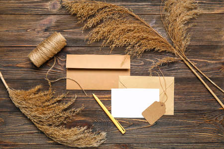 Envelopes with blank card, tag, pen and pampas grass on dark wooden backgroundの写真素材