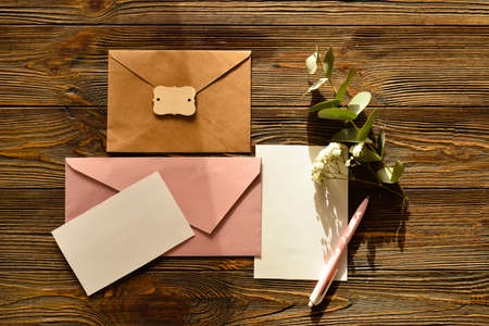 Envelopes with blank cards, flowers and eucalyptus branch on wooden backgroundの写真素材