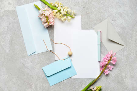 Envelopes with blank cards, flowers and pen on light background