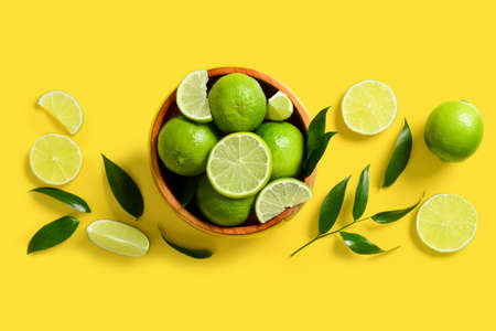 Composition with bowl of ripe limes and leaves on yellow background