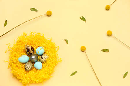 Nest with painted Easter eggs, flowers and green leaves on yellow backgroundの写真素材
