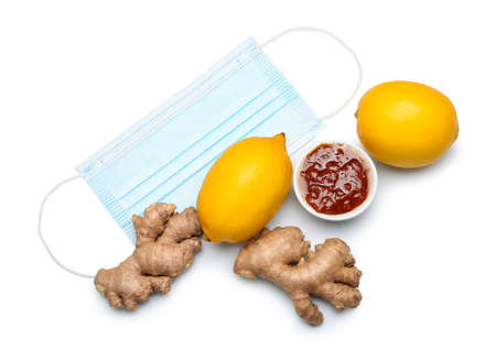 Lemons with jam, ginger and medical mask on white background. Sore throat conceptの写真素材