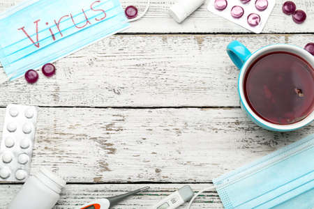 Frame made of medical mask with word VIRUS, tea cup, thermometers and medications for sore throat on white wooden backgroundの写真素材