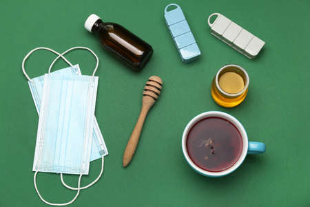 Cup of tea, pills for sore throat, syrup, honey and medical masks on green backgroundの写真素材