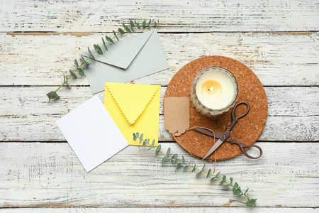 Envelopes with card, scissors, candle and eucalyptus branches on white wooden backgroundの写真素材