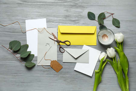 Envelopes with cards, candle, scissors, tulips and eucalyptus leaves on gray wooden backgroundの写真素材